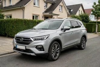 SUV familial de marque chinoise garé dans un quartier résidentiel européen, vue 3/4 avant sur carrosserie argentée moderne